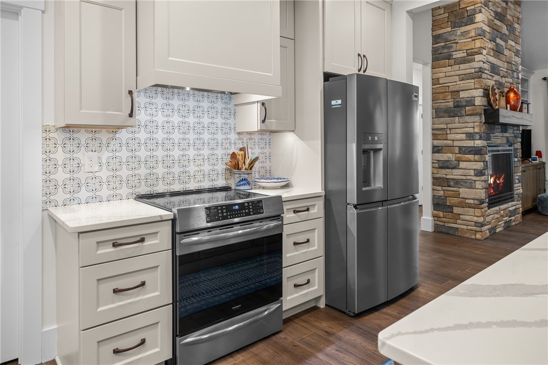 113 South Oak Pointe Drive Seneca, SC 29672 - Photo 14 of 50 This kitchen showcases elegant cabinetry, modern appliances, and a beautiful tiled backsplash, with a stone fireplace nearby.