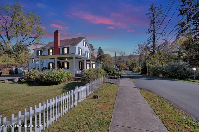 a view of a white house next to a road with big trees