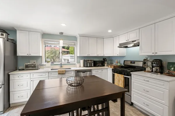 a kitchen with a stove a sink dishwasher a refrigerator with white cabinets and wooden floor