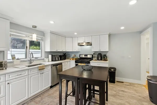 a kitchen with a sink a stove a refrigerator and white cabinets with wooden floor