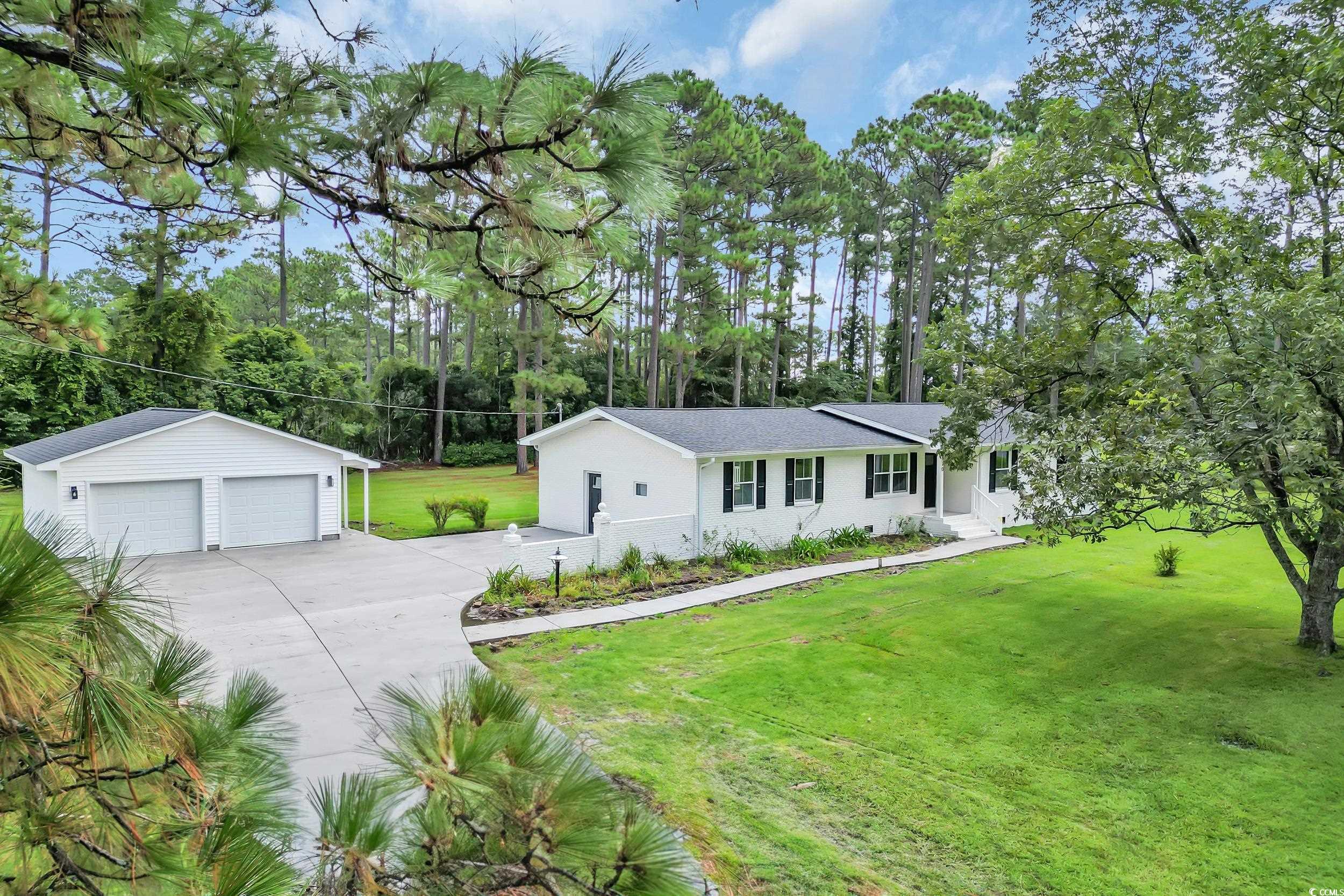 Single story home featuring a garage, a front yard, an outbuilding, and view of scattered trees