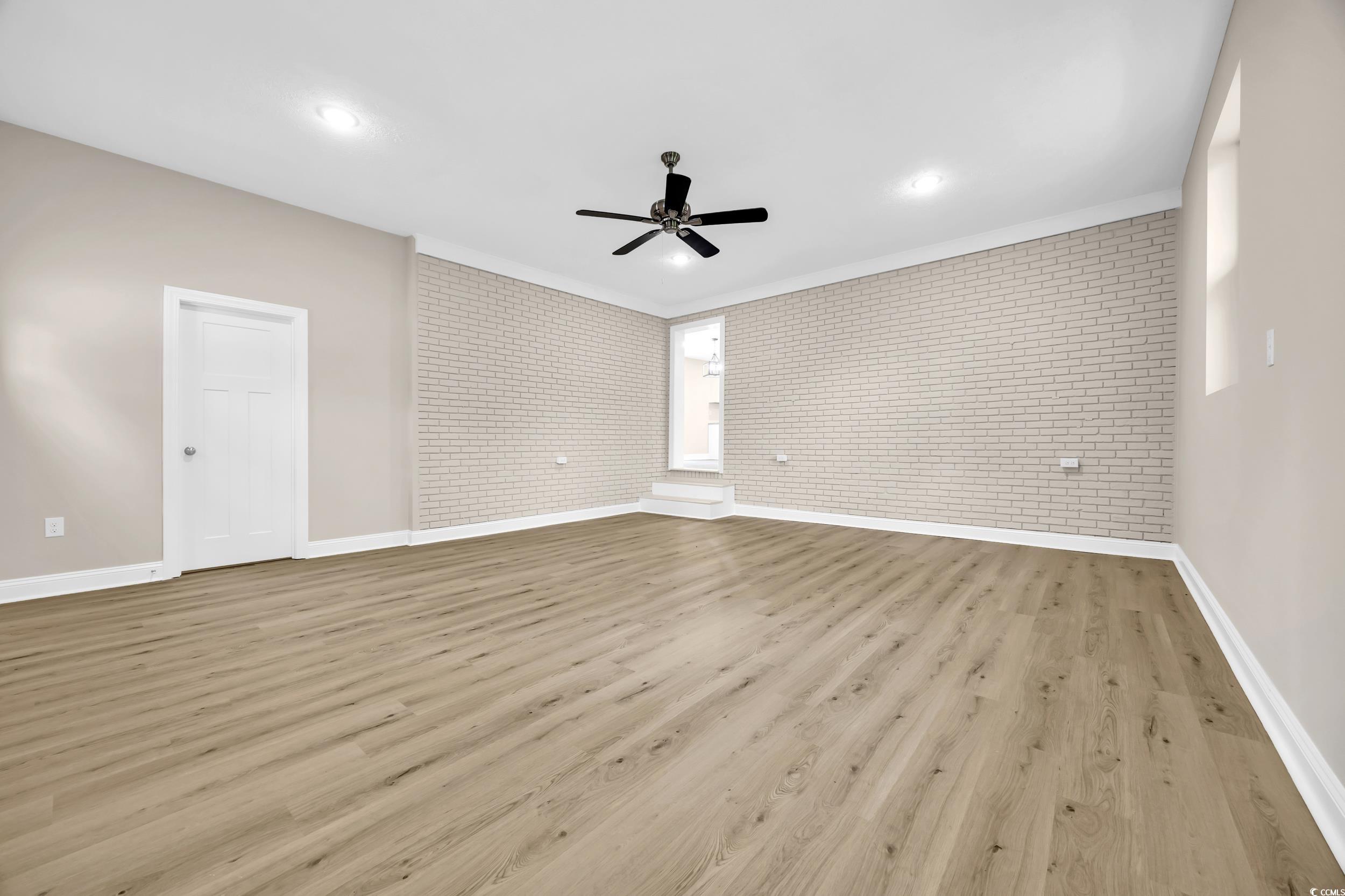 970 Virginia Drive Loris, SC 29569 - Photo 11 of 28 Unfurnished living room featuring light wood-type flooring, brick wall, a ceiling fan, and crown molding