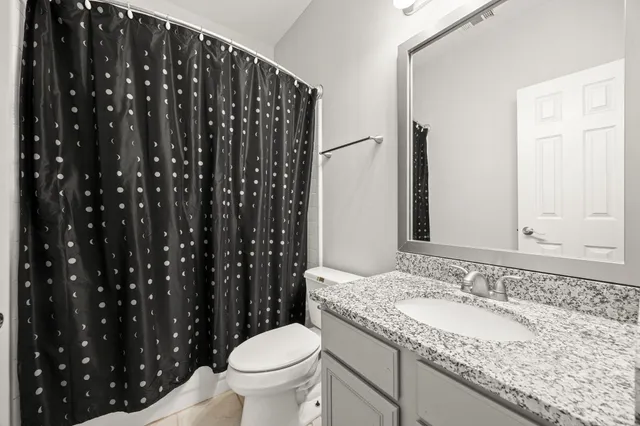 a bathroom with a granite countertop sink a toilet a mirror and shower curtain