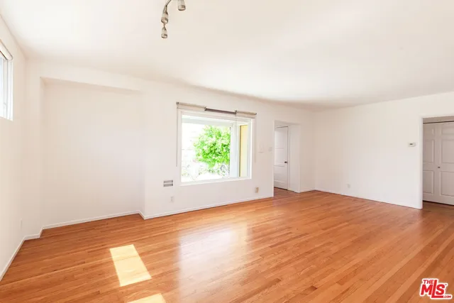a view of an empty room with wooden floor and a window