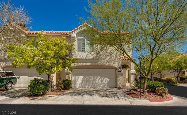A terracotta-tiled roof and white stucco facade define this inviting two-story residence, framed by vibrant trees.