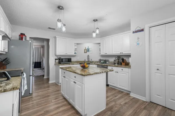 a kitchen with granite countertop a refrigerator a stove top oven a sink dishwasher and white cabinets with wooden floor