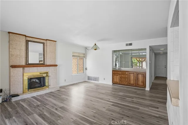 a view of an empty room with wooden floor fireplace and a window