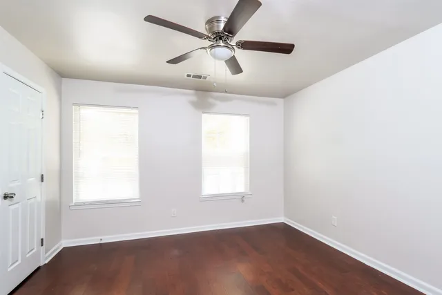 an empty room with wooden floor ceiling fan and windows