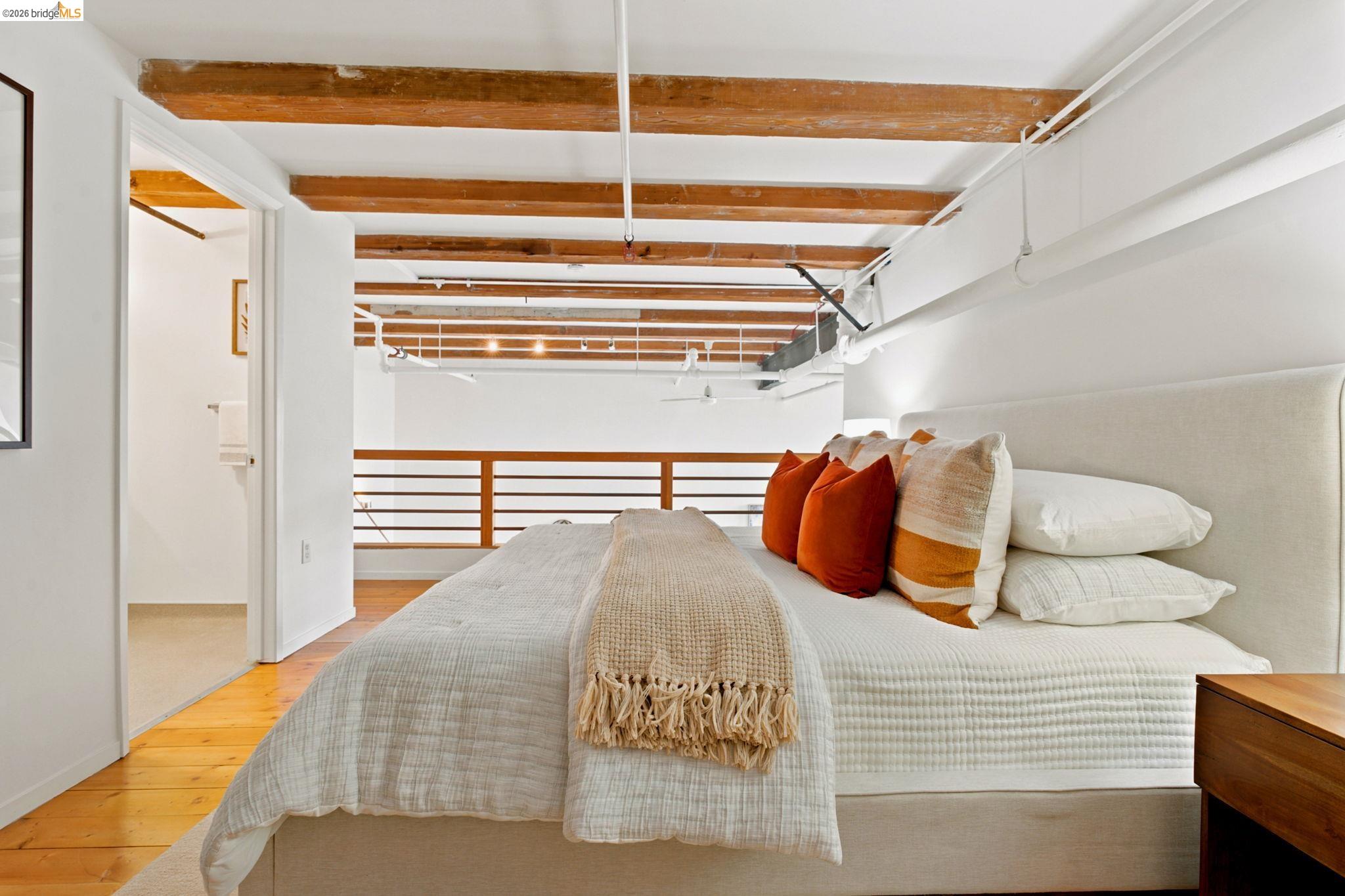 1920 Union Street, Unit 9 Oakland, CA 94607 - Photo 24 of 35 Bedroom featuring exposed wood ceiling beams, wood-finish flooring, a contemporary upholstered headboard, and a wood railing overlooking the lower level