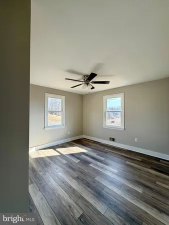 an empty room with wooden floor ceiling fan and windows