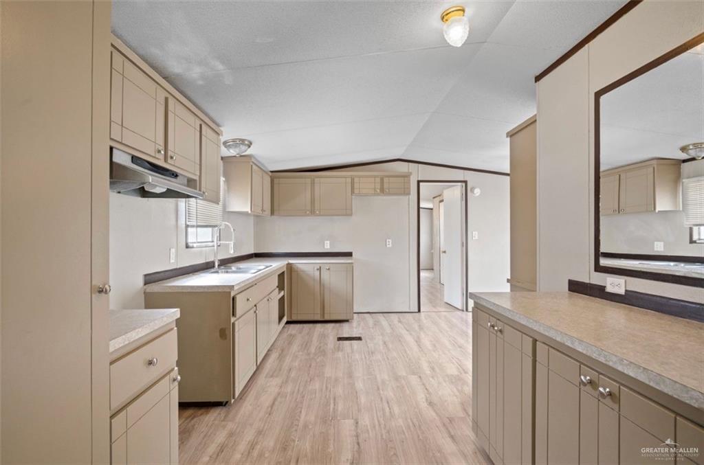 115 East Which Way Pharr, TX 78577 - Photo 6 of 20 Kitchen with light wood-style floors, vaulted ceiling, under cabinet range hood, and light countertops