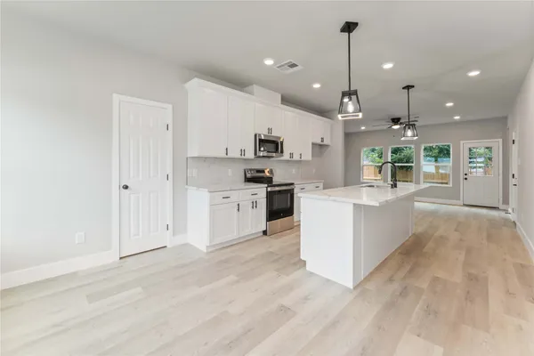 a large white kitchen with lots of counter space a sink appliances and cabinets
