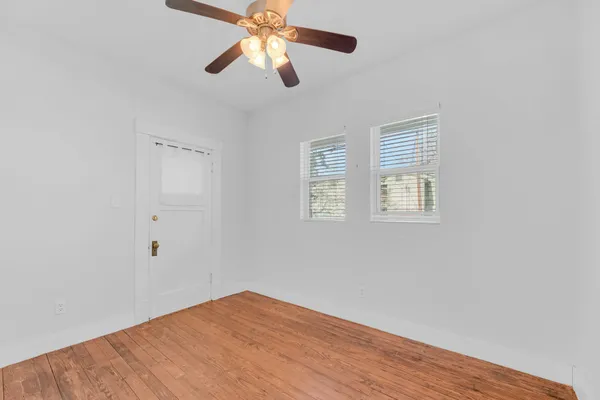 an empty room with wooden floor fan and windows