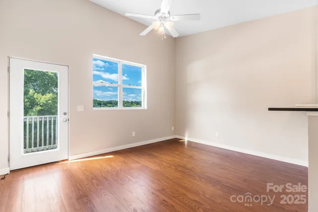 an empty room with wooden floor chandelier fan and windows
