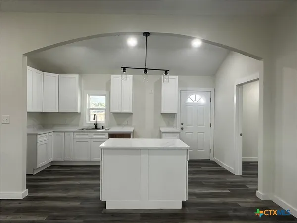 a large white kitchen with kitchen island a sink dishwasher a stove and a refrigerator with wooden floor