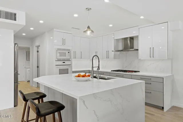 a kitchen with stainless steel appliances a sink a stove a refrigerator and white cabinets with wooden floor