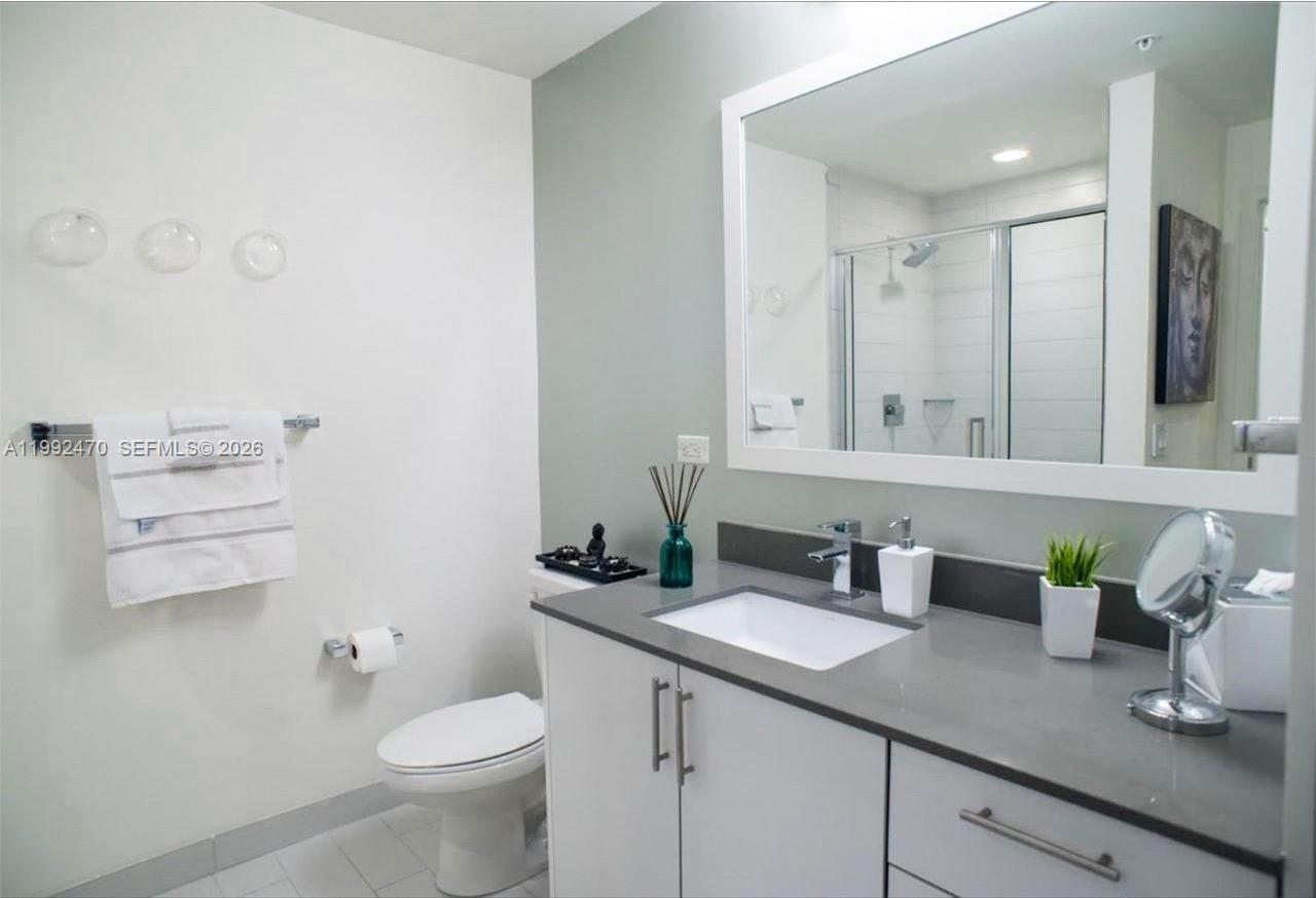 999 Southwest 1st Avenue, Unit 3208 Miami, FL 33130 - Photo 12 of 14 a bathroom with a granite countertop sink a toilet and a mirror