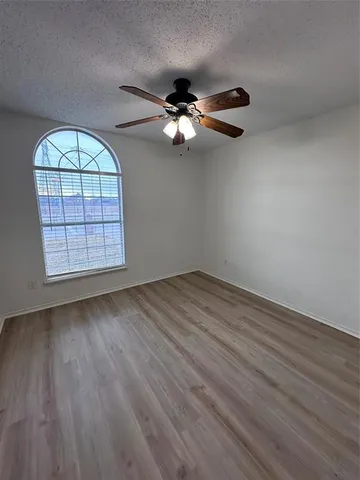 an empty room with wooden floor chandelier fan and windows