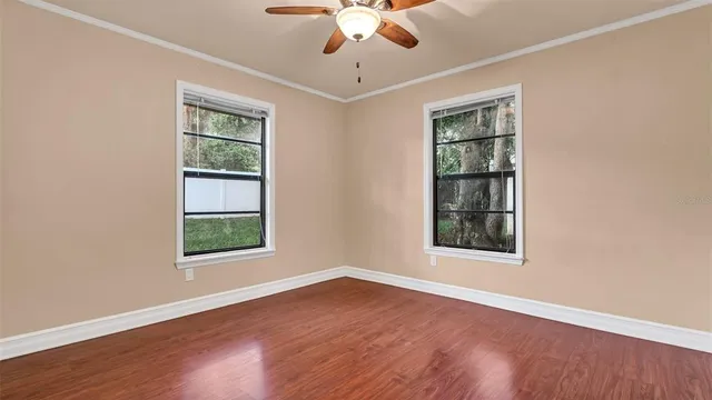 an empty room with wooden floor chandelier and windows