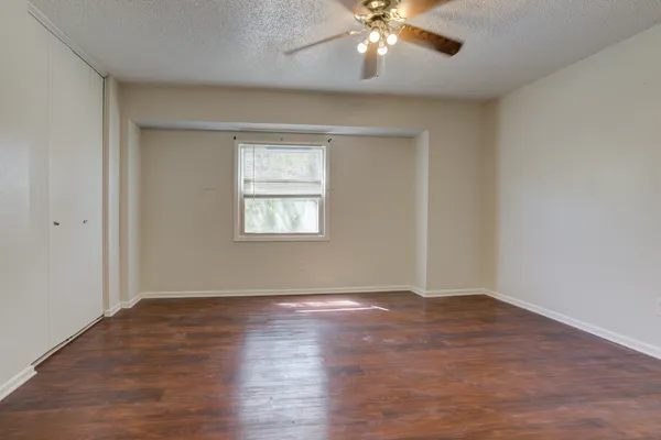 an empty room with wooden floor chandelier fan and windows