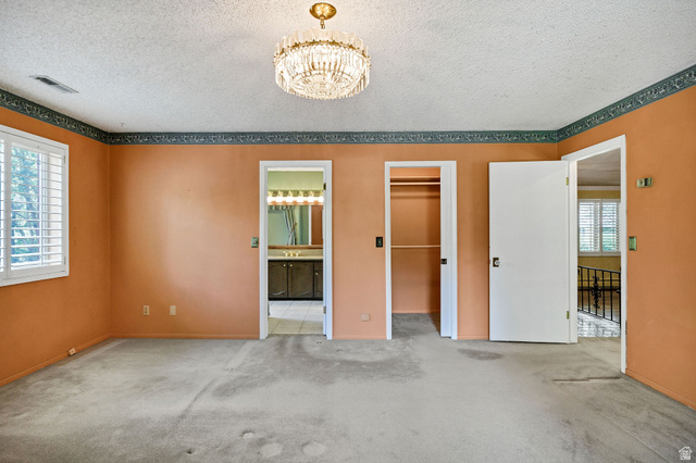 1365 Sumac Drive Logan, UT 84321 - Photo 28 of 66 Carpeted interior room featuring a decorative chandelier, white plantation shutters, an open doorway revealing a bathroom vanity with multiple light fixtures, and a second open doorway showcasing a closet with shelving