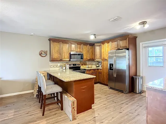 a kitchen with stainless steel appliances granite countertop a refrigerator a sink dishwasher a stove with wooden cabinets and wooden floor