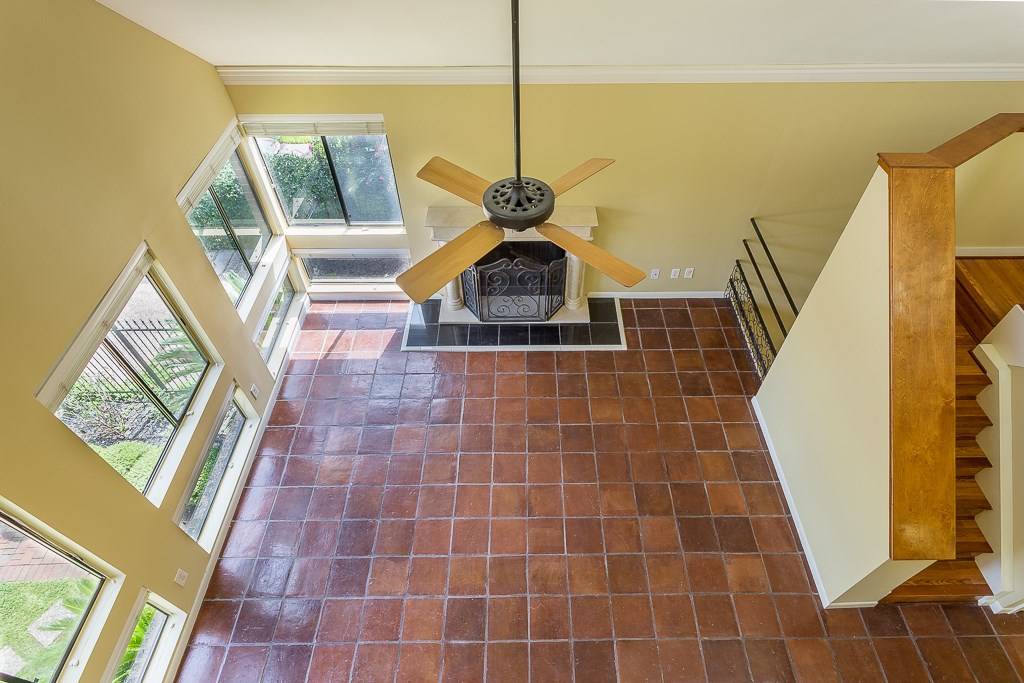 2349 Albans Road, Unit 2 Houston, TX 77005 - Photo 6 of 25 Spacious living area with large windows, terracotta floor tiles, and a central ceiling fan. The room includes a cozy fireplace and a staircase with wooden railings, adding warmth and character.