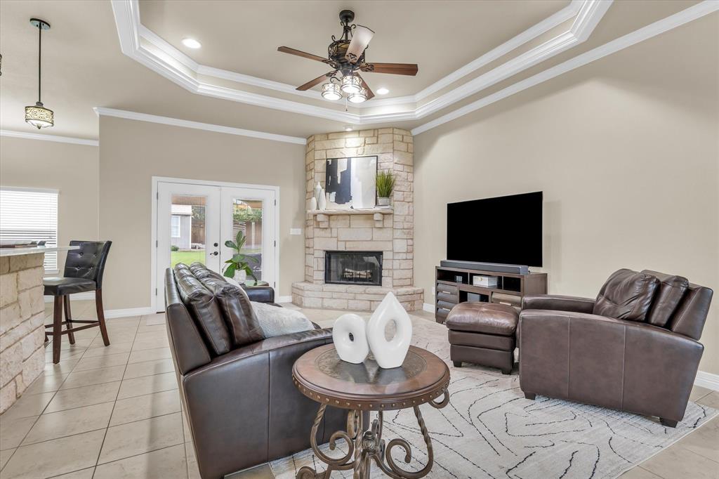 910 Springdale Lane Lorena, TX 76655 - Photo 6 of 39 Living area featuring a stone-clad fireplace and mantle, tray ceiling with crown molding, and a ceiling fan