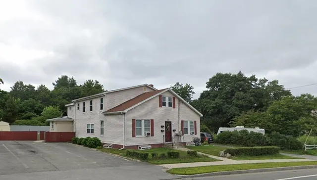 a view of a white house next to a yard with big trees