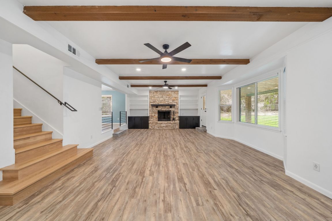 2175 Park Road New Braunfels, TX 78132 - Photo 4 of 39 Unfurnished living room with a stone fireplace, a ceiling fan, light wood-style flooring, stairs, and beam ceiling