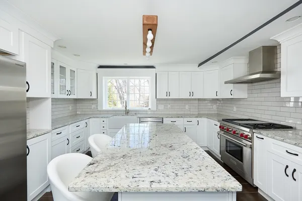 a large kitchen with granite countertop a stove a sink a window and white cabinets