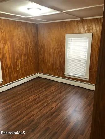 an empty room with wooden floor and windows with curtains