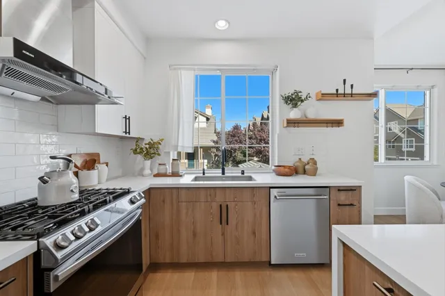 a kitchen with stainless steel appliances a sink dishwasher a refrigerator and a dining table with wooden floor