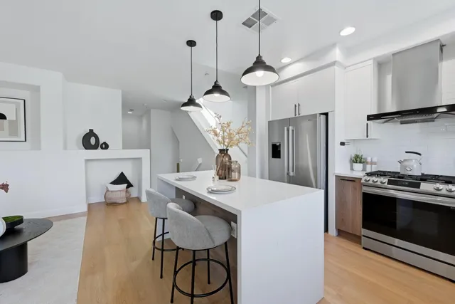 a kitchen with stainless steel appliances granite countertop a refrigerator a sink dishwasher a dining table and chairs with wooden floor