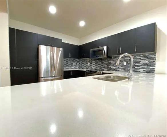 a view of kitchen with stainless steel appliances kitchen island granite countertop a refrigerator and a sink