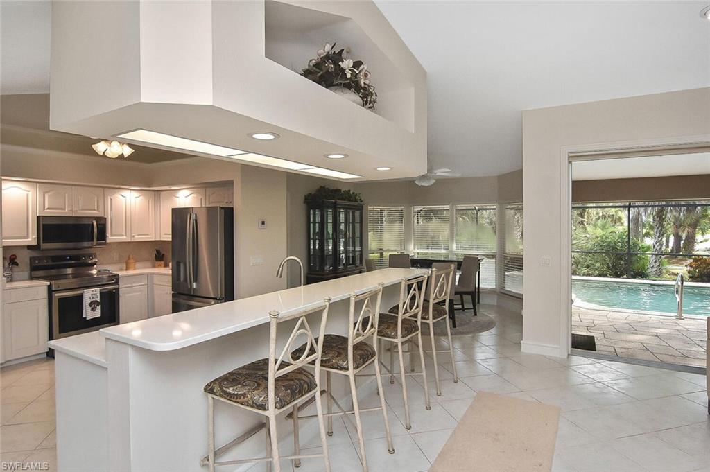 8928 Lely Island Circle Naples, FL 34113 - Photo 9 of 44 a kitchen with stainless steel appliances granite countertop a stove top oven a sink dishwasher a dining table and chairs with wooden floor