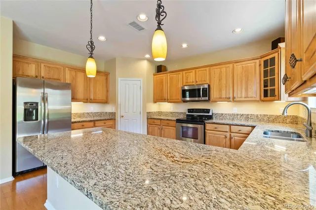 a kitchen with stainless steel appliances granite countertop a sink a stove top oven a refrigerator with wooden cabinets