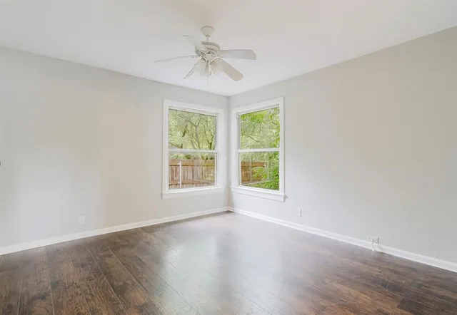 an empty room with wooden floor fan and windows