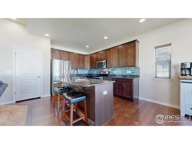 a kitchen with stainless steel appliances kitchen island granite countertop a refrigerator a stove a sink a dining table and chairs with wooden floor