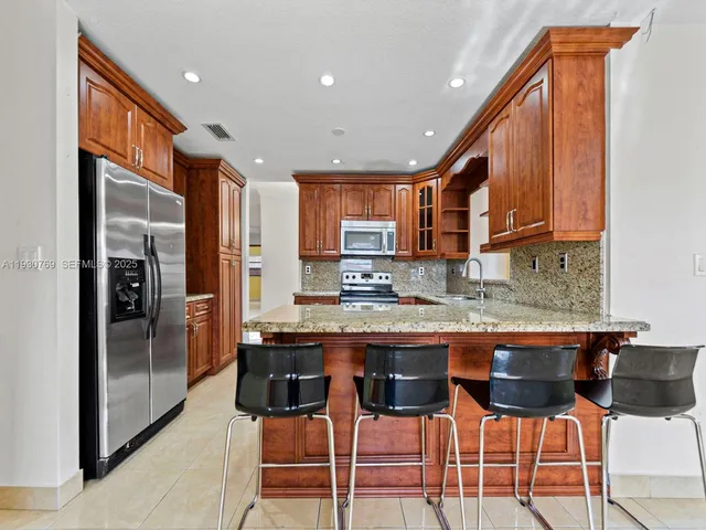 a kitchen with stainless steel appliances granite countertop a stove top oven a refrigerator a sink and chairs