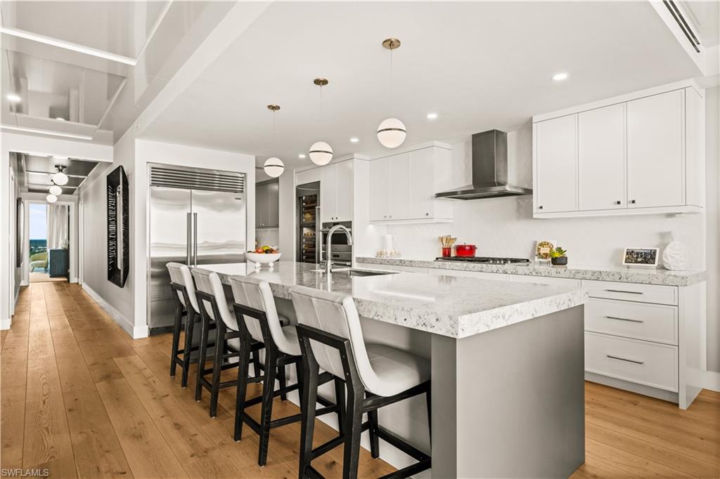 13925 Old Coast Road, Unit 1705 Naples, FL 34110 - Photo 13 of 42 Kitchen featuring white cabinetry, light wood-style floors, decorative light fixtures, a kitchen breakfast bar, and a large island
