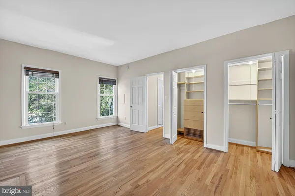 an empty room with wooden floor closet and windows