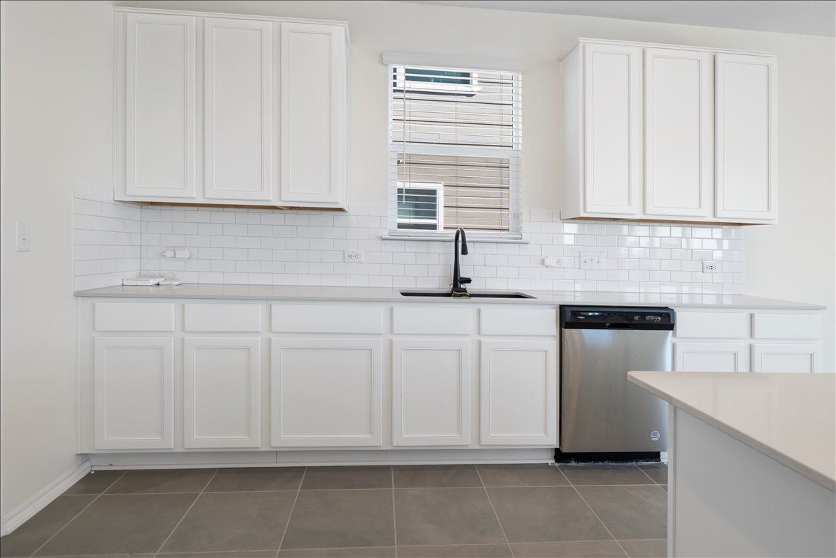 18501 Spotted Eagle Lane Elgin, TX 78621 - Photo 10 of 40 A well-appointed kitchen showcasing white cabinetry, sleek countertops, and a modern sink under a sun-filtering window.