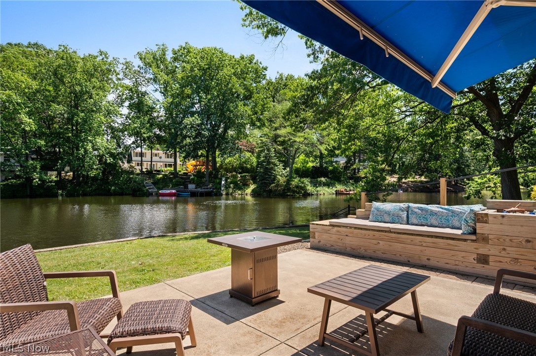 685 Sunnyside Road Vermilion, OH 44089 - Photo 3 of 50 Expansive concrete patio with built-in wood bench seating, waterfront access, and a retractable blue awning