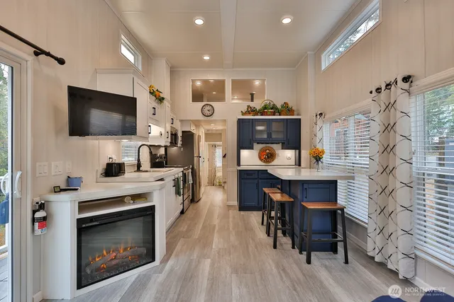 a living room with stainless steel appliances furniture a fireplace a flat screen tv and kitchen view