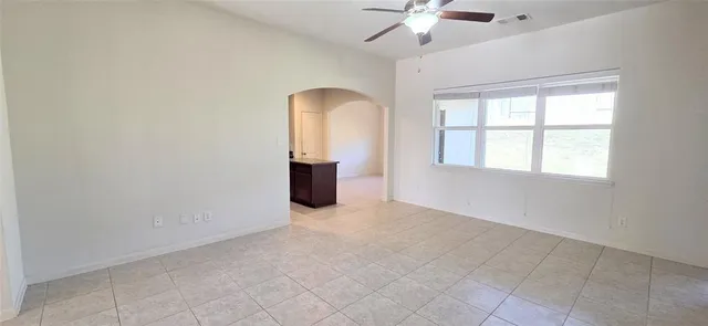 an empty room with chandelier fan and windows