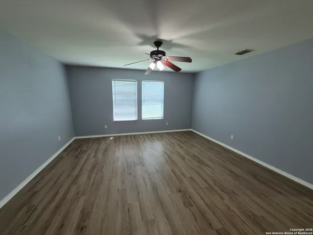 an empty room with wooden floor ceiling fan and windows