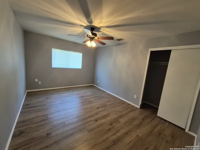 an empty room with wooden floor fan and windows