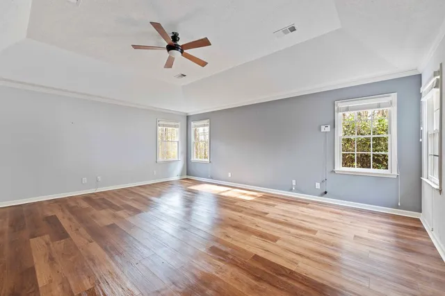 an empty room with wooden floor fan and windows