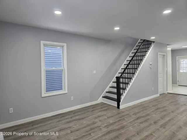 a view of an empty room with wooden floor stairs and windows